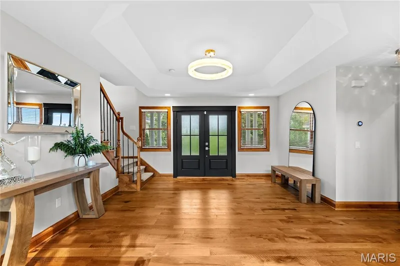 Hardwood flooring throughout, coffered ceiling detail, recessed lighting, double entry doors with glass panels, and a staircase with wood treads and wrought iron balusters — 205 Howell Road, Defiance, MO 63341