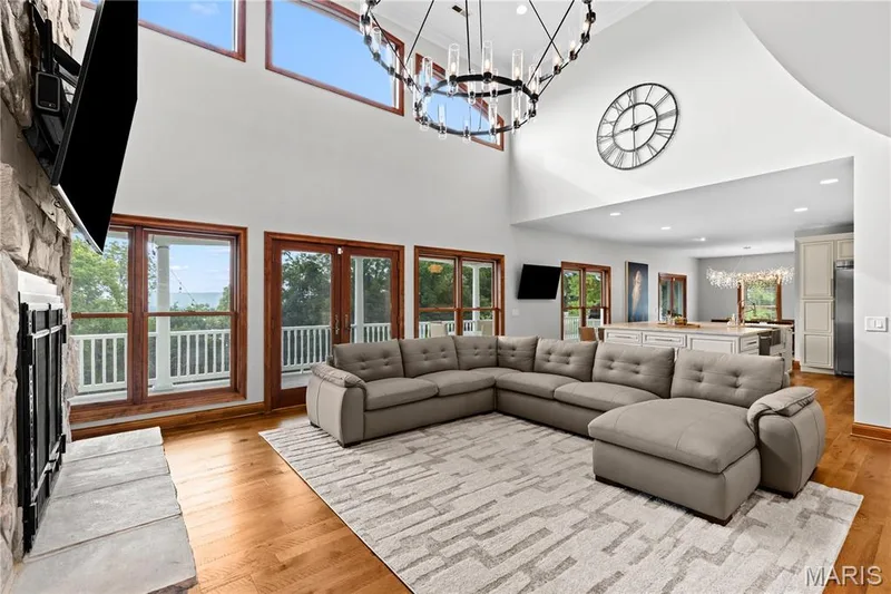 Vaulted ceilings with clerestory windows, large format transom windows, wood-finish flooring, stone-clad fireplace, and a contemporary chandelier — 205 Howell Road, Defiance, MO 63341