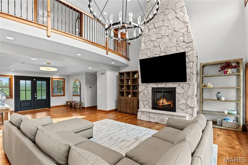Two-story stone-clad fireplace with hearth, wood-finish flooring, and a second-story interior balcony with wood and wrought iron railings — 205 Howell Road, Defiance, MO 63341