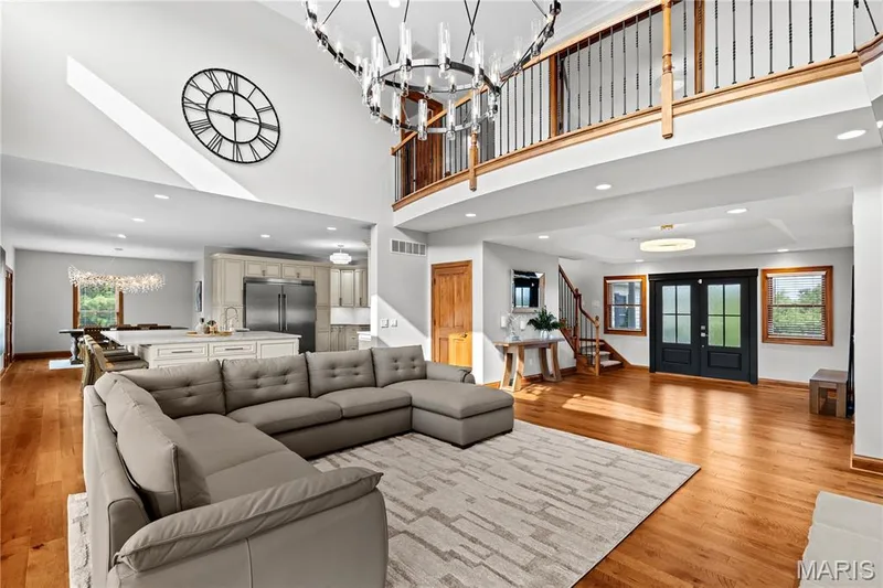 Vaulted ceiling with a large chandelier, wood-finish flooring, kitchen with stainless steel appliances, white cabinetry, and a double-door entry — 205 Howell Road, Defiance, MO 63341