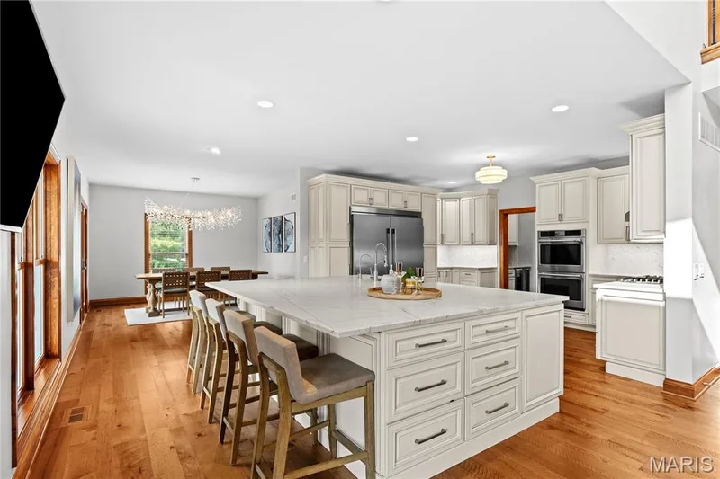 Expansive kitchen featuring a large central island with seating, stainless steel appliances, abundant cabinetry, and wood-finish flooring — 205 Howell Road, Defiance, MO 63341