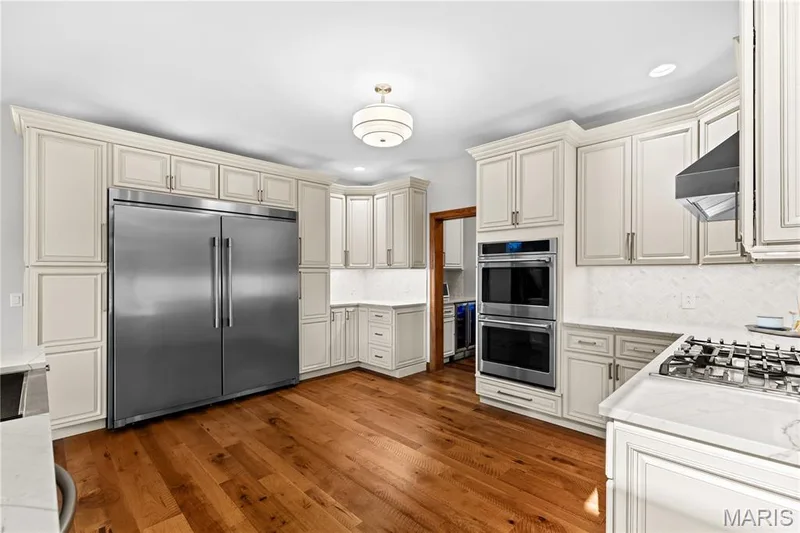 White cabinetry with crown molding, stainless steel appliances, wood-finish flooring, white countertops, and a white tile backsplash — 205 Howell Road, Defiance, MO 63341