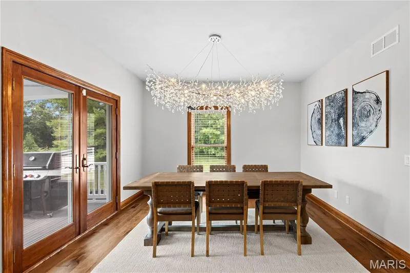 Hardwood flooring, wood trim, glass-paneled double doors, window with blinds, and an ornate chandelier — 205 Howell Road, Defiance, MO 63341