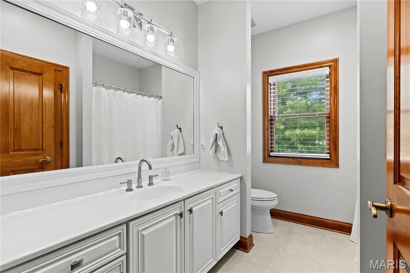 Double vanity featuring a light-toned countertop with an undermount sink, brushed nickel faucet, and white cabinetry — 205 Howell Road, Defiance, MO 63341