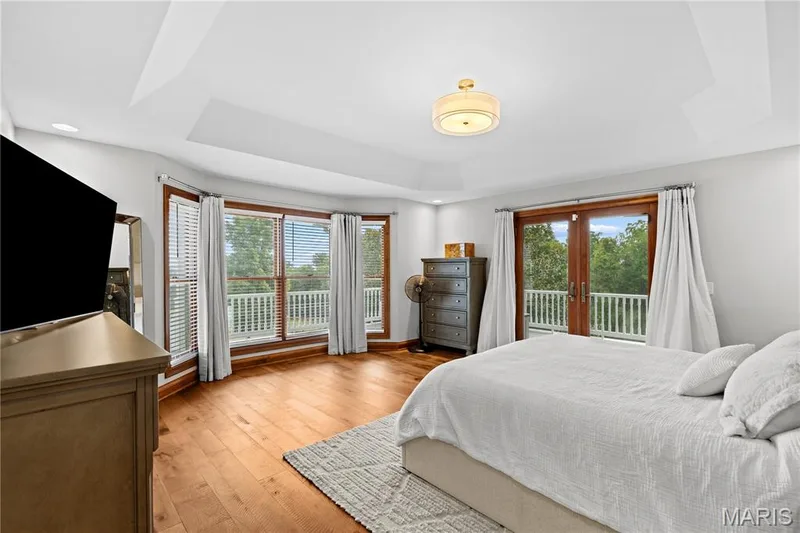 Recessed lighting, tray ceiling, wood-finish flooring, bay window with blinds, and double doors to a balcony — 205 Howell Road, Defiance, MO 63341