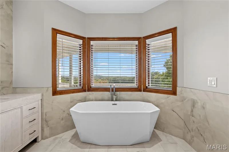 Freestanding soaking tub with a floor-mounted faucet, surrounded by large format wall and floor tiling — 205 Howell Road, Defiance, MO 63341