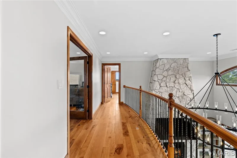 Hardwood flooring, crown molding, recessed lighting, stone-clad fireplace, and an open railing with wood and wrought iron elements — 205 Howell Road, Defiance, MO 63341
