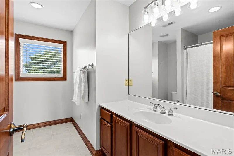 White vanity with an integrated sink and chrome faucet, large frameless mirror, and a window with wood-finish trim — 205 Howell Road, Defiance, MO 63341