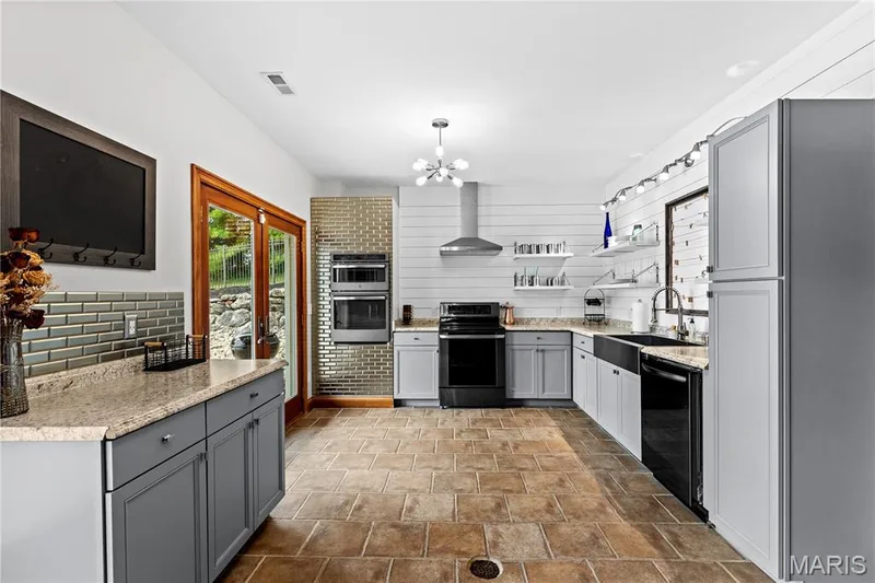 Tiled flooring, double wall ovens, stainless steel range hood, ample cabinetry, and granite-style countertops — 205 Howell Road, Defiance, MO 63341