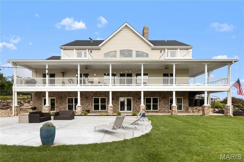 Two-story exterior featuring a stone and siding facade, a covered upper-level balcony, a lower-level patio, and a manicured lawn — 205 Howell Road, Defiance, MO 63341