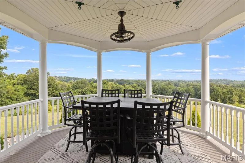 Covered outdoor living space featuring white columns and railing, a wood-finish floor, and a built-in ceiling fan — 205 Howell Road, Defiance, MO 63341