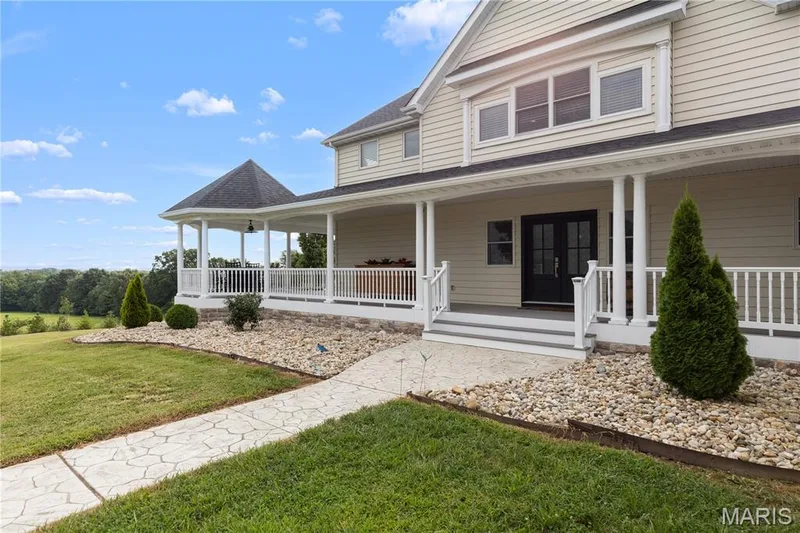 Expansive covered front porch with white railing, featuring a hexagonal gazebo and gray composite steps — 205 Howell Road, Defiance, MO 63341