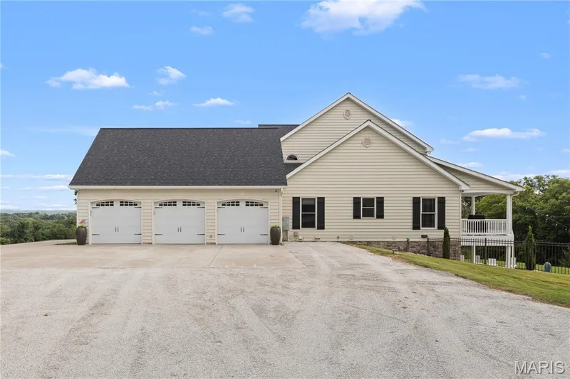 Exterior featuring light-colored siding, black shutters, and a three-car garage with arched window details — 205 Howell Road, Defiance, MO 63341