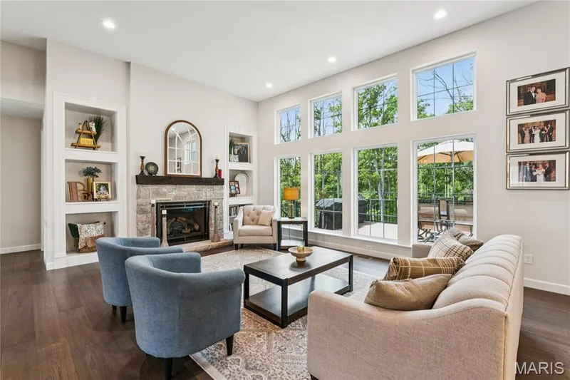Vaulted ceiling with recessed lighting, stone fireplace with a wood mantle, built-in shelving, wood-finish flooring, and expansive windows — 5 Timberdel Place, Foristell, MO 63348