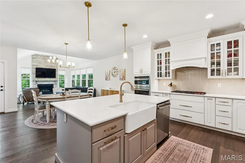 Kitchen featuring white cabinetry, a center island with a farmhouse sink, stainless steel appliances, and light-toned countertops — 5 Timberdel Place, Foristell, MO 63348