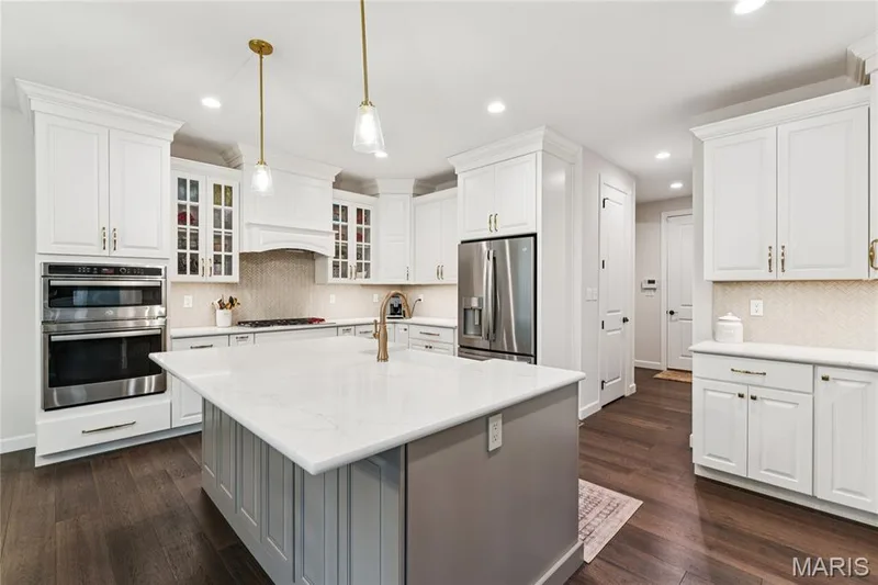 Gourmet kitchen featuring white cabinetry, stainless steel double ovens, a large center island with a light-toned countertop, wood-finish flooring, and recessed lighting — 5 Timberdel Place, Foristell, MO 63348
