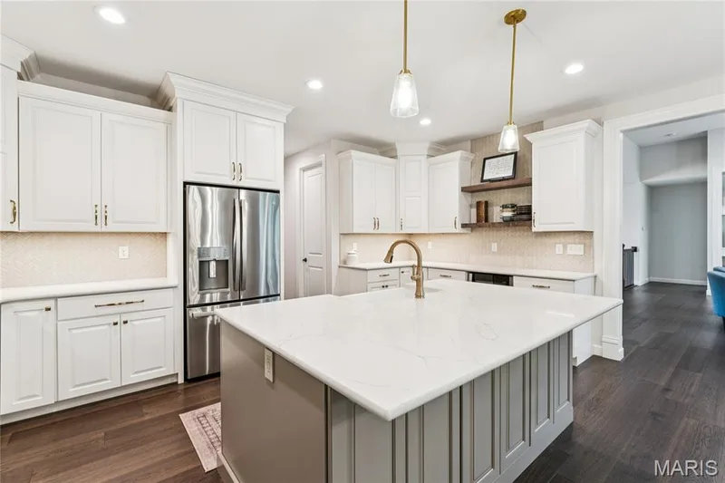 White cabinetry, stainless steel refrigerator, center island with stone countertop, gold-tone hardware, and wood-finish flooring — 5 Timberdel Place, Foristell, MO 63348