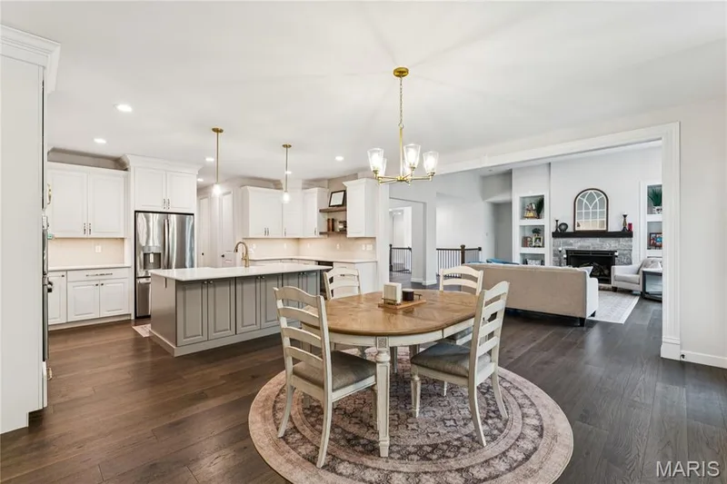 Open-concept living space with dark wood-finish flooring, a kitchen island with gray cabinetry, a built-in fireplace with a stone surround, and recessed lighting throughout — 5 Timberdel Place, Foristell, MO 63348