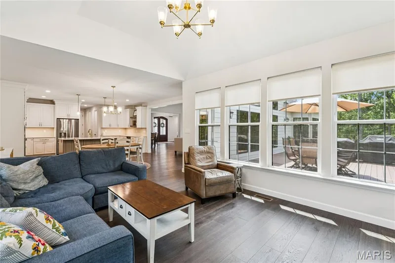 Open-concept living space featuring high vaulted ceilings, dark wood-finish flooring, and ample natural light from multiple large windows — 5 Timberdel Place, Foristell, MO 63348