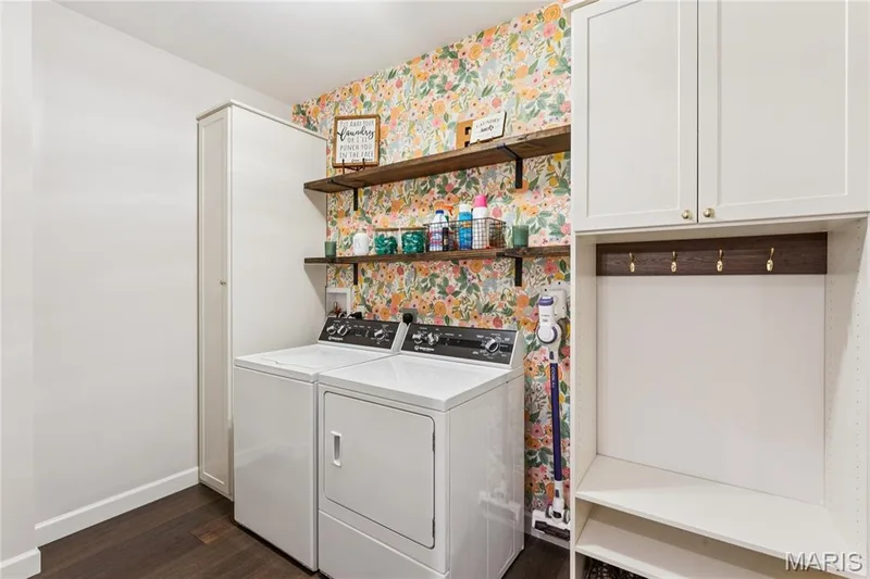Laundry area featuring white cabinetry, wood-finish flooring, floral-patterned wall covering, open shelving with metal brackets, and built-in coat hooks — 5 Timberdel Place, Foristell, MO 63348