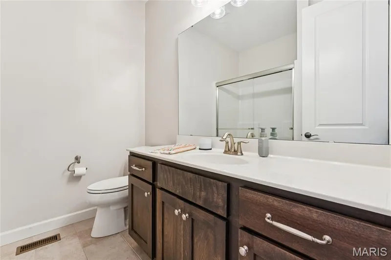 Dark wood-finish vanity with a light-toned countertop, a single basin sink, and a large wall-mounted mirror — 5 Timberdel Place, Foristell, MO 63348