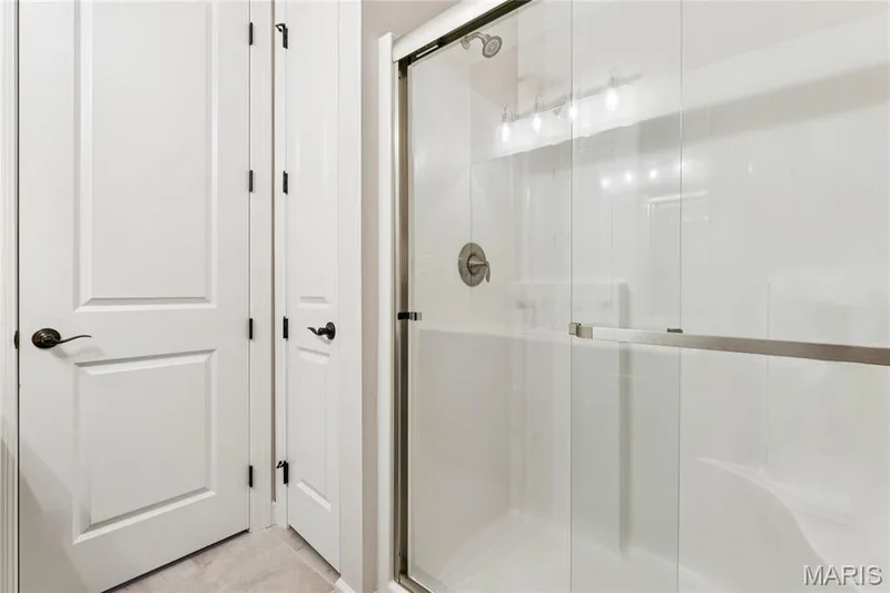 Glass-enclosed shower with a brushed nickel showerhead and fixture, white shower walls, and a multi-bulb vanity light — 5 Timberdel Place, Foristell, MO 63348