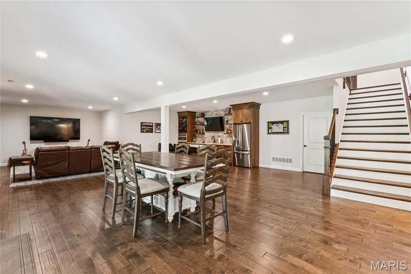 Luxury vinyl throughout, featuring a built-in bar/kitchen with wood cabinetry, microwave/oven combo, quartz countertops and stainless steel appliances, and a staircase with wood treads and handrail — 5 Timberdel Place, Foristell, MO 63348