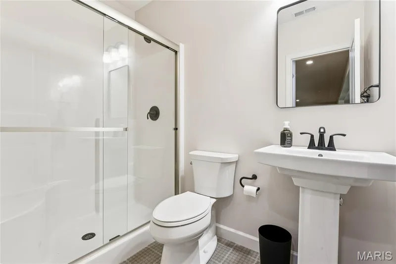 Glass-enclosed shower with matte black fixtures, white pedestal sink, and rectangular framed mirror, tile flooring — 5 Timberdel Place, Foristell, MO 63348