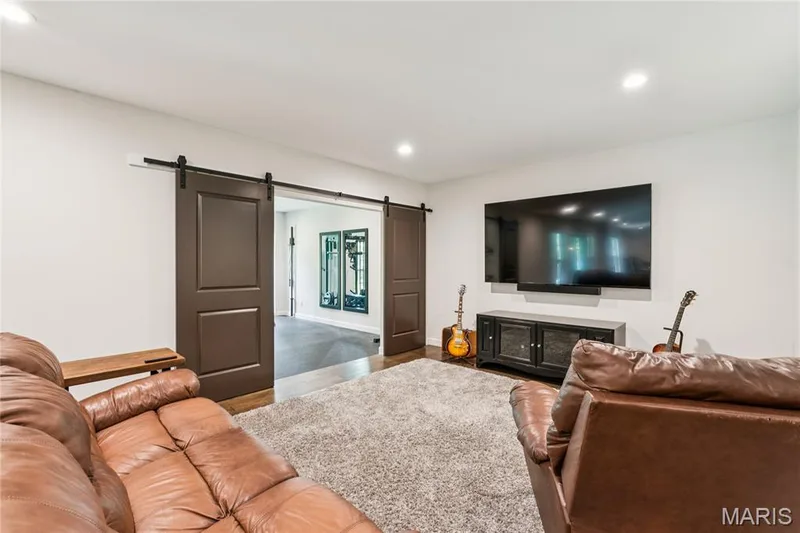 Barn door entry to an additional space, recessed lighting, and a wall-mounted media console — 5 Timberdel Place, Foristell, MO 63348