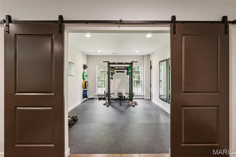 Dual barn doors with dark hardware, recessed lighting, double windows, rubber flooring, and full-length wall mirrors — 5 Timberdel Place, Foristell, MO 63348