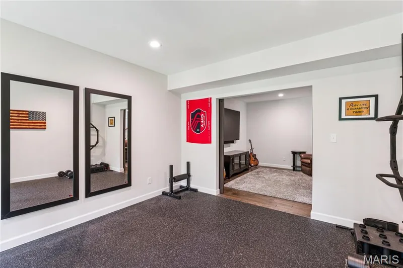 Recessed lighting, light gray wall color, two full-length mirrors with black frames, dark rubber flooring, wood-finish flooring in adjacent area — 5 Timberdel Place, Foristell, MO 63348