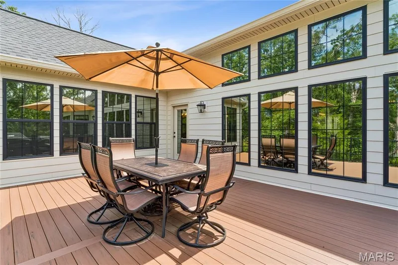 Expansive wood-finish 16 x 24 deck with a beige siding exterior and multiple large windows with black frames — 5 Timberdel Place, Foristell, MO 63348
