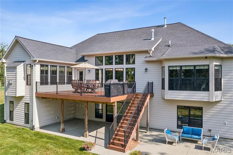 Multi-level exterior with a large upper deck featuring dark railings, a full-length staircase, and a lower-level concrete patio — 5 Timberdel Place, Foristell, MO 63348
