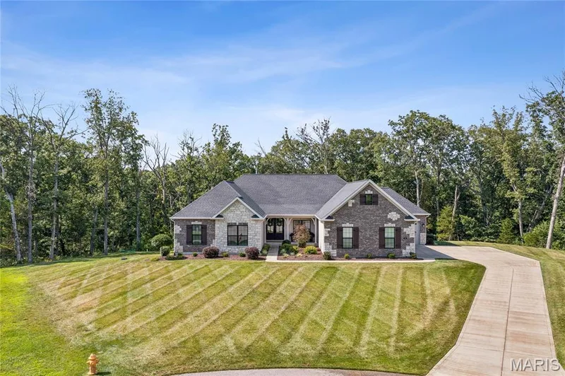 Brick and stone exterior with dark shutters, gabled roofline, and an attached garage — 5 Timberdel Place, Foristell, MO 63348