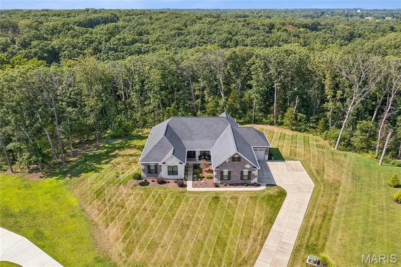 Expansive 3-acre property featuring a large residence with a multi-gabled roof, extensive surrounding greenery, and a paved driveway — 5 Timberdel Place, Foristell, MO 63348