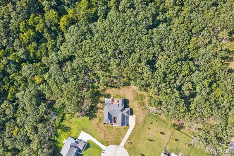 Aerial perspective showcasing a cul-de-sac, expansive wooded area, and manicured lawns — 5 Timberdel Place, Foristell, MO 63348