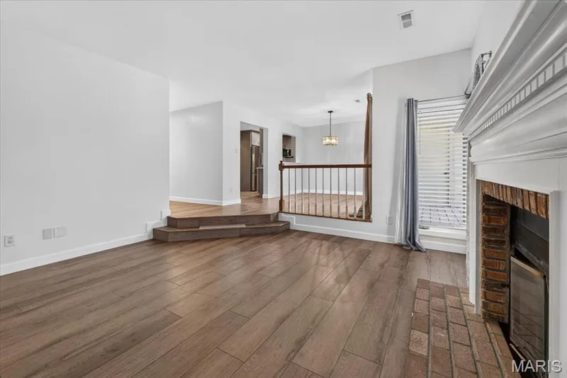 Wood-finish flooring throughout, white painted walls, white fireplace mantel, brick fireplace surround, and built-in window blinds — 1608 Lake Knoll Drive #1A, Lake St. Louis, MO 63367
