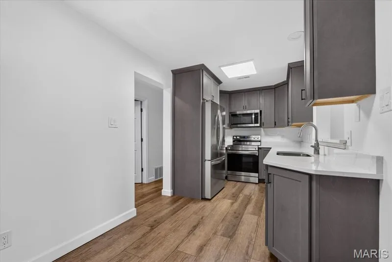 Kitchen featuring wood-finish flooring, gray cabinetry, white countertops, and stainless steel appliances — 1608 Lake Knoll Drive #1A, Lake St. Louis, MO 63367