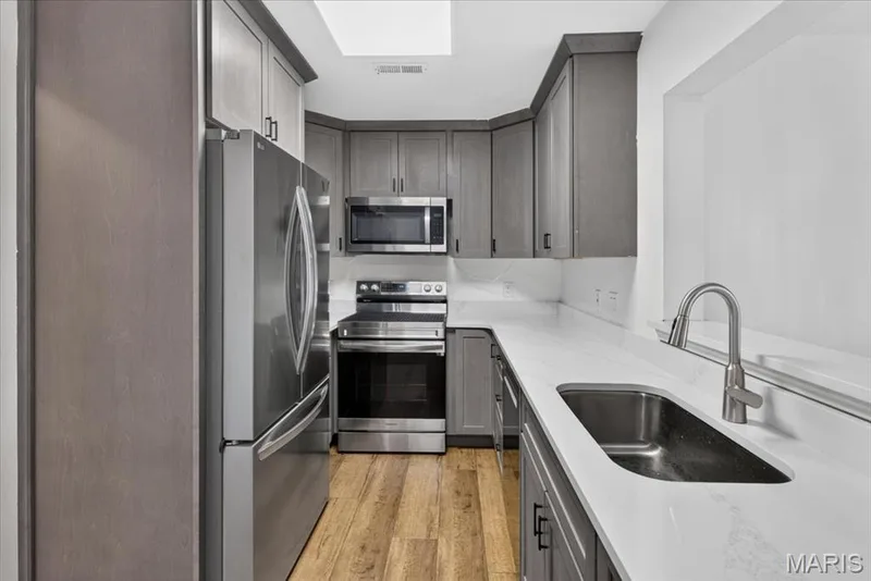 Kitchen featuring stainless steel appliances, wood-finish flooring, grey cabinetry, white countertops, and a skylight — 1608 Lake Knoll Drive #1A, Lake St. Louis, MO 63367