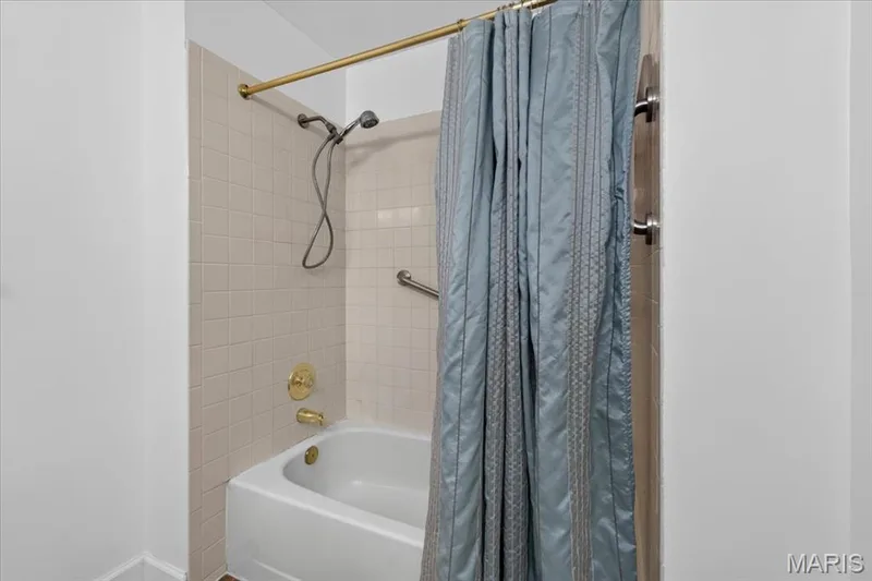 White bathtub with brass fixtures, a handheld showerhead, and tile surround — 1608 Lake Knoll Drive #1A, Lake St. Louis, MO 63367