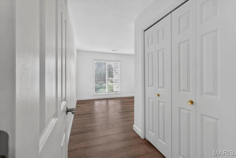 Bright interior with wood-finish flooring, white walls, and a large window with horizontal blinds — 1608 Lake Knoll Drive #1A, Lake St. Louis, MO 63367