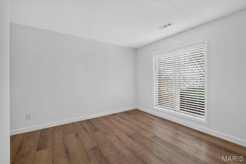 Bright corner room featuring pristine white walls, recessed ceiling lighting, and warm wood-finish flooring — 1608 Lake Knoll Drive #1A, Lake St. Louis, MO 63367