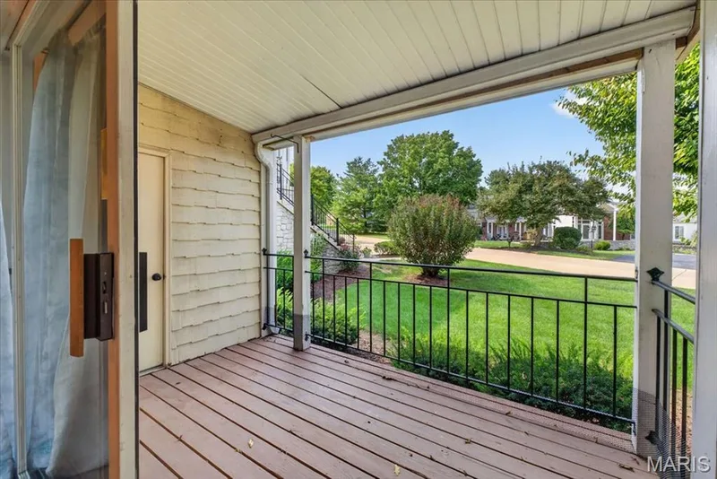 Covered porch featuring wood-finish decking, black metal railing, and shingle siding — 1608 Lake Knoll Drive #1A, Lake St. Louis, MO 63367
