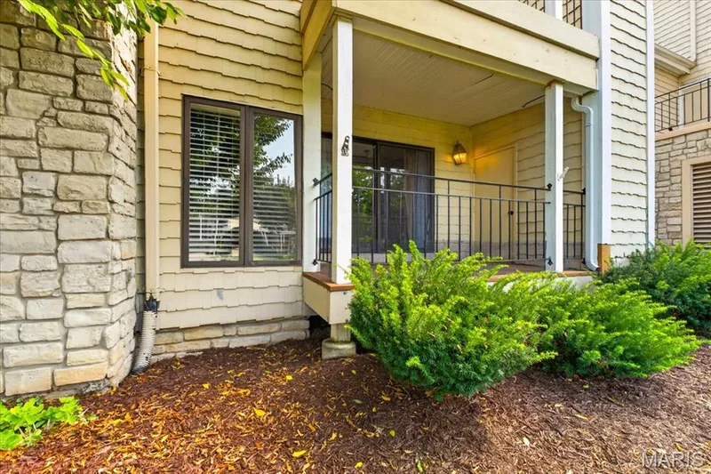 Front porch entry featuring a covered pavilion with white columns, black shuttered windows, and stone exterior cladding — 1608 Lake Knoll Drive #1A, Lake St. Louis, MO 63367