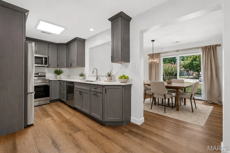 Kitchen featuring grey cabinetry, stainless steel appliances, white countertops, and wood-finish flooring. Digitally enhanced and virtually staged. — 1608 Lake Knoll Drive #1A, Lake St. Louis, MO 63367