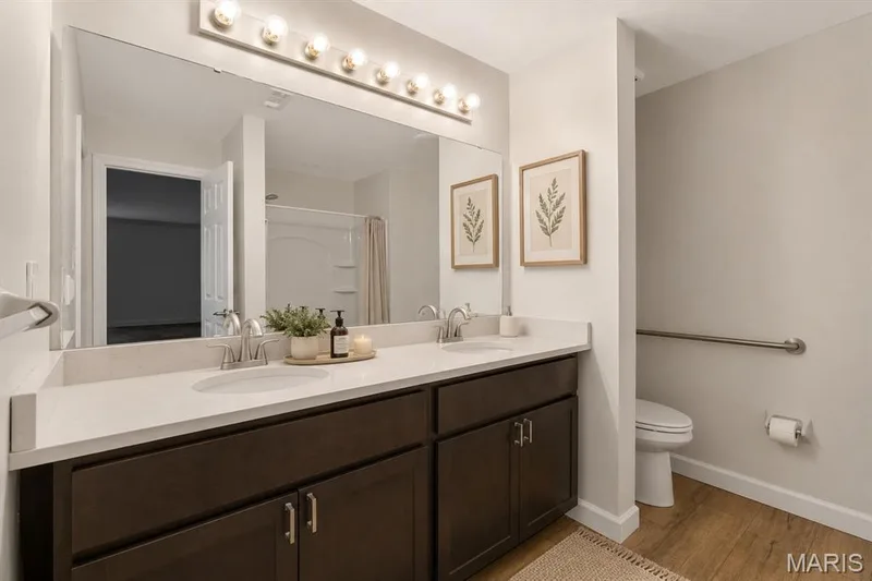 Dual vanity with dark wood-finish cabinetry, light-toned countertop, and undermount sinks. Digitally enhanced and virtually staged. — 1608 Lake Knoll Drive #1A, Lake St. Louis, MO 63367