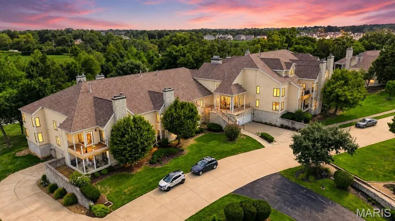 Multi-level residence featuring multiple balconies, extensive paved driveways, stone chimney accents, and mature landscaping — 1608 Lake Knoll Drive #1A, Lake St. Louis, MO 63367