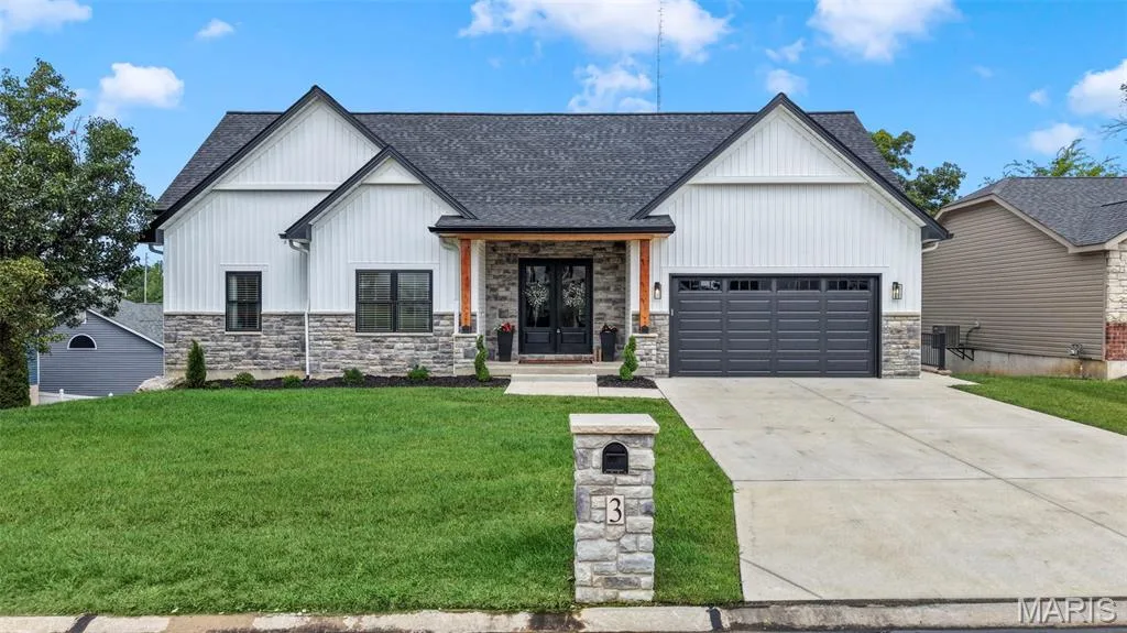 Contemporary exterior featuring white board and batten siding, stone facade accents, a dark shingle roof, a prominent front entry, and a two-car garage — 3 Millers Court, O'Fallon, MO 63366