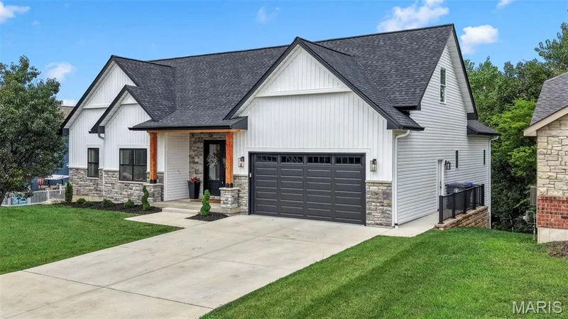 Modern farmhouse residence featuring a striking white vertical-board exterior with stone accents, peaked rooflines with architectural gables, and a charcoal gray two-car garage door — 3 Millers Court, O'Fallon, MO 63366