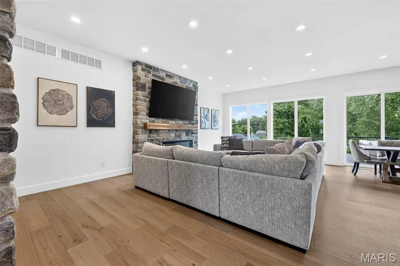 Bright, open-concept living space featuring hardwood flooring, a gas fireplace with stone surround, and a wall-mounted flat-screen television — 3 Millers Court, O'Fallon, MO 63366